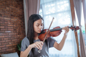 Girl playing violin showcasing the benefits of music and how it helps reduce stress.