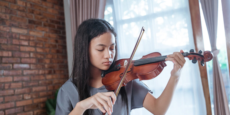 Girl playing violin showcasing the benefits of music and how it helps reduce stress.